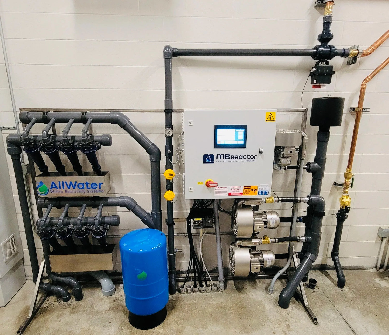Water treatment system with pipes and a control panel on a tiled wall. This is Allwater equipment